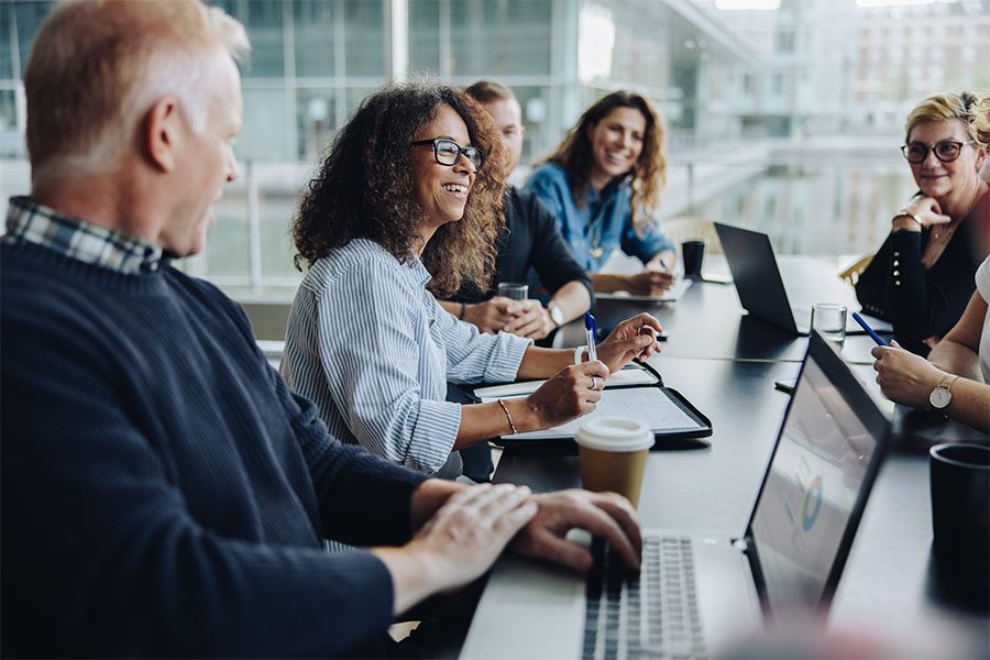 About Our Agency - View of Cheerful Group of Coworkers Sitting Around a Table During a Business Meeting in the Office