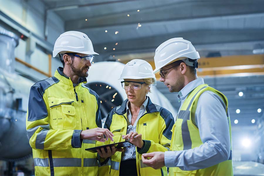 Insurance Quote - Group of Engineers Standing in a Manufacturing Facility Having a Discussion While Using a Tablet